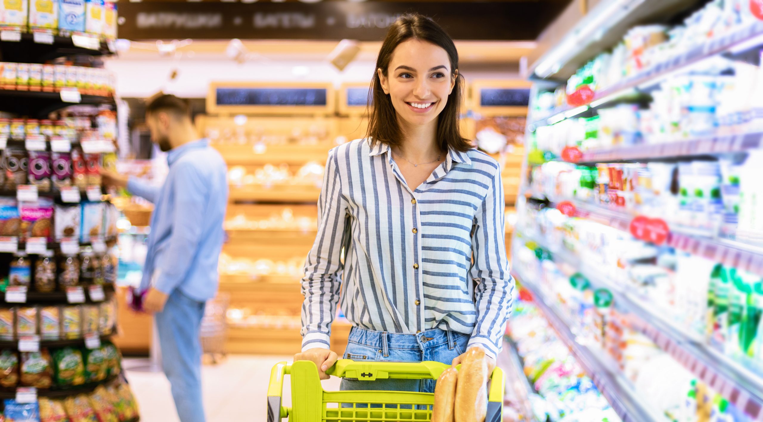 Woman in grocery store pushing cart full of food.