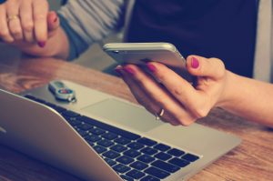 Woman holding iPhone over laptop.